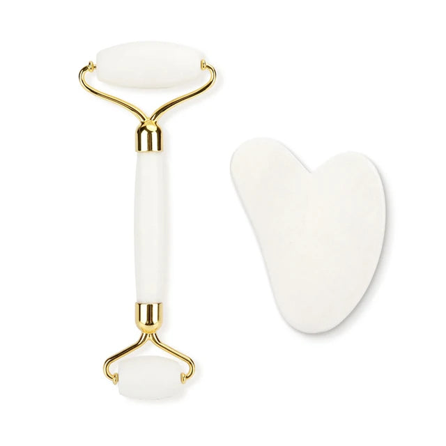 White facial roller with gold accents and a heart-shaped white tool on a white background